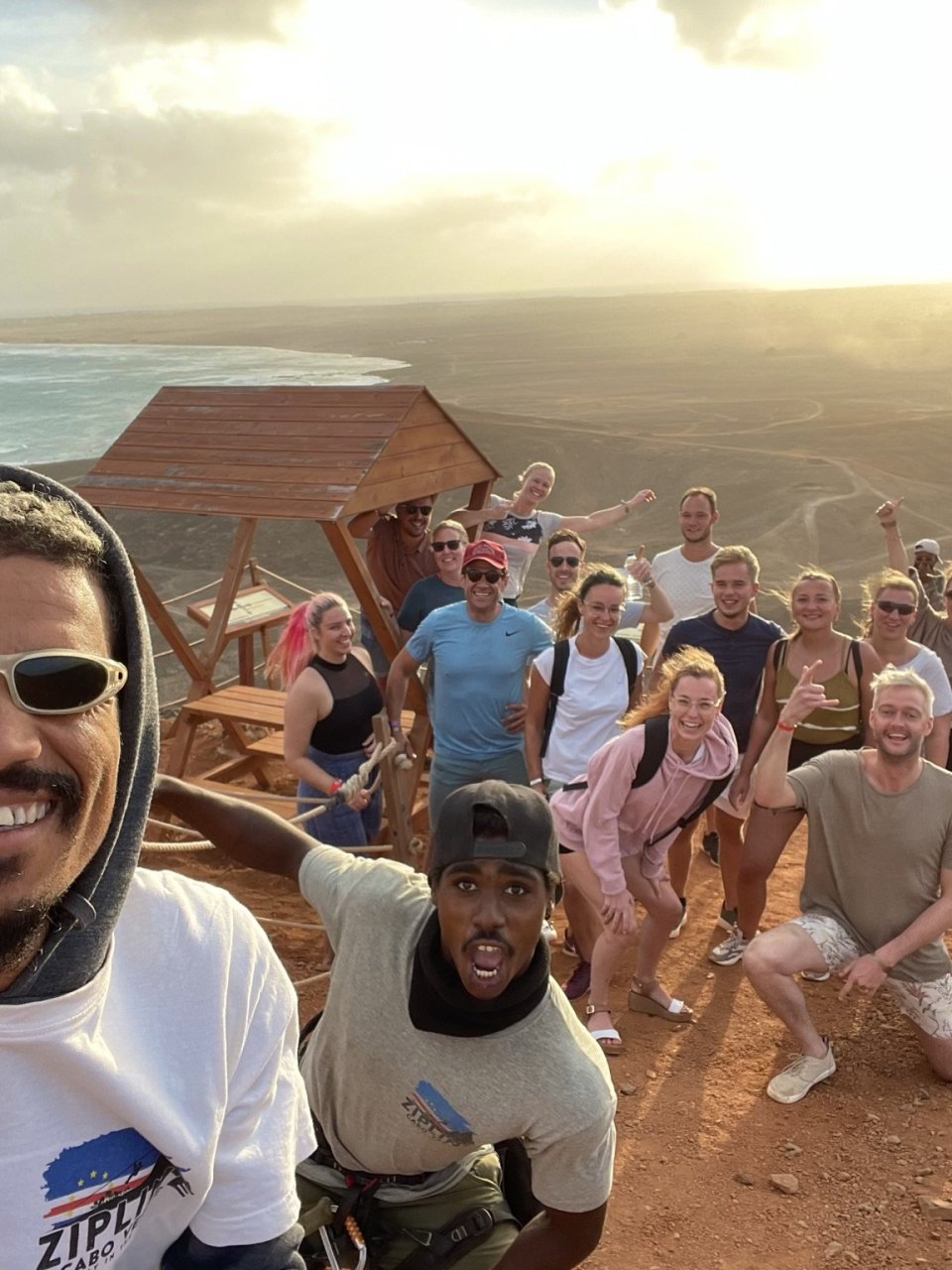 Groep reisgenoten poseert samen met hun gids bij een uitzichtpunt over de kust en het woestijnlandschap.