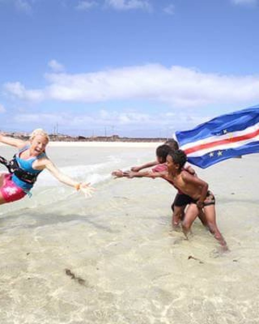 Kitesurfer krijgt hulp in het ondiepe water terwijl de Kaapverdische vlag wappert.