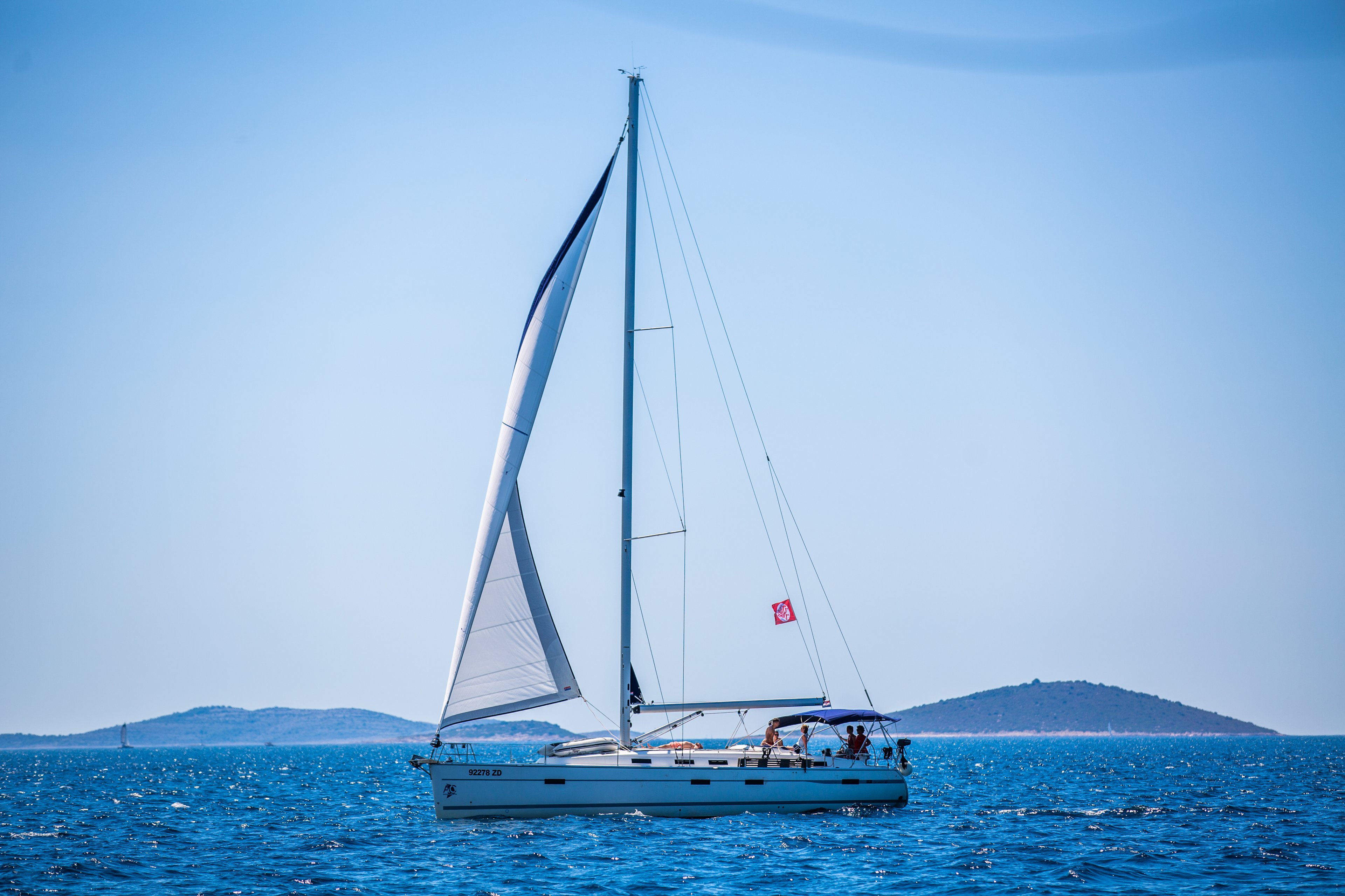 Zeilboot vaart over het helderblauwe water met de Kroatische kust op het achtergrond.