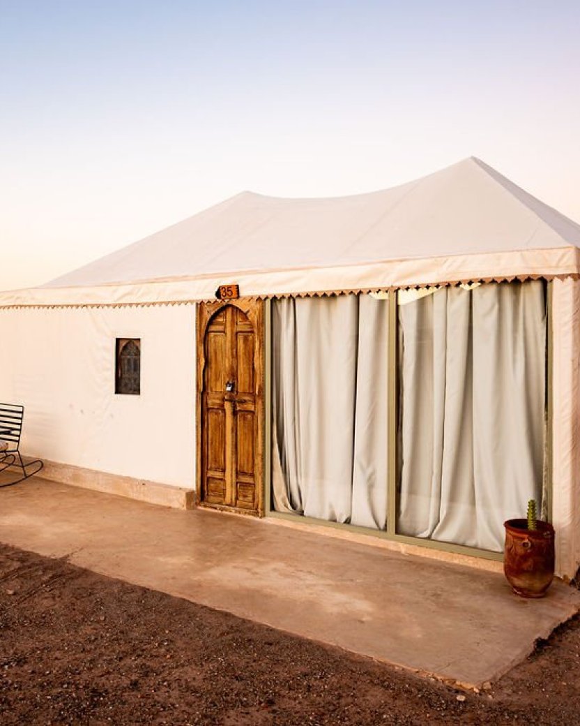 Witte glampingtent in de woestijn bij zonsondergang.