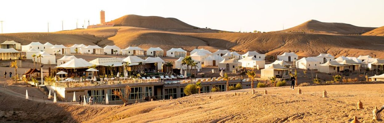 Luxe woestijnresort met witte tenten en heuvels op de achtergrond.