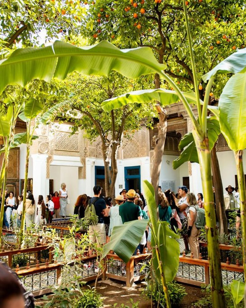 Reisgenoten bezoeken samen een groene binnenplaats van een paleis met palmbomen en traditionele architectuur in Marokko.