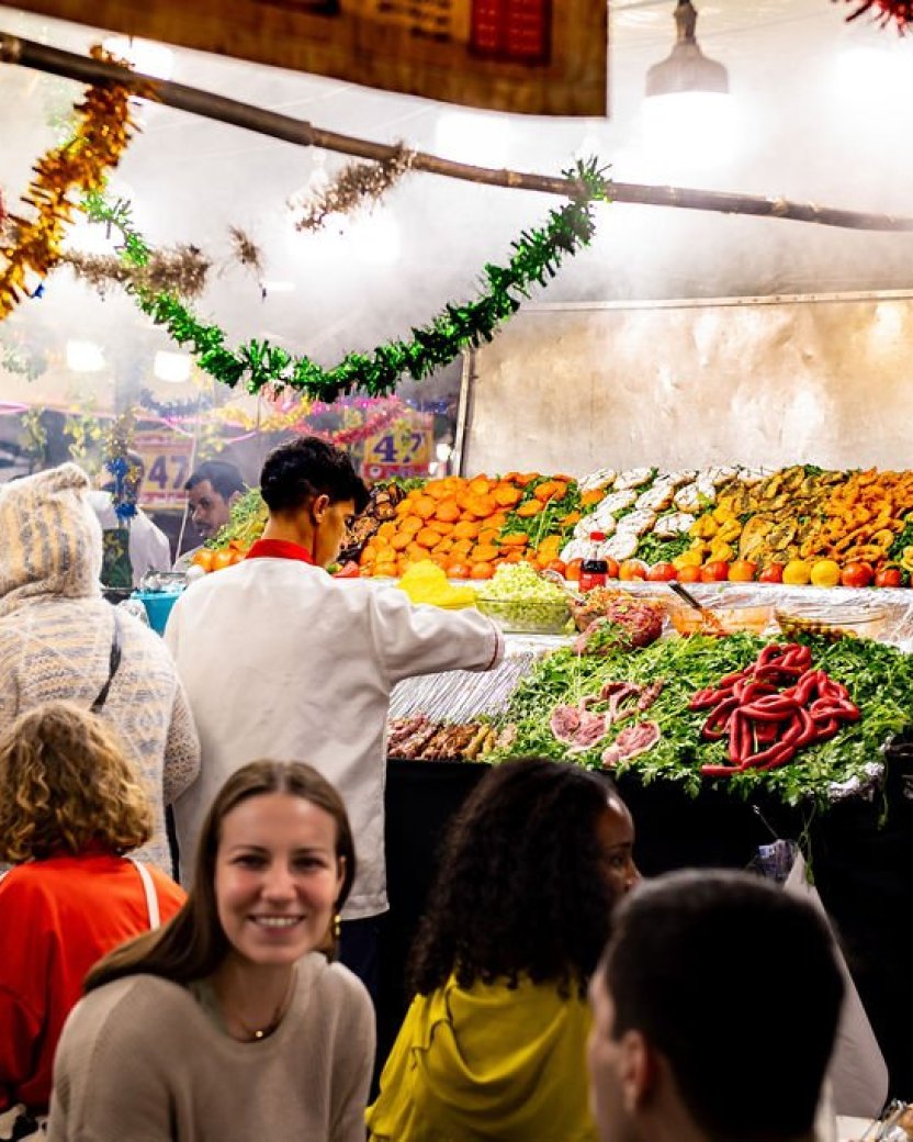 Reisgenoten eten samen op een levendige Marokkaanse markt met kraampjes vol lokale gerechten.