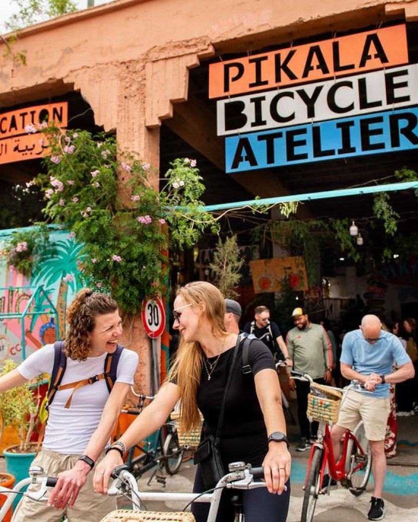 Reisgenoten stappen op de fiets bij een kleurrijke fietsenwerkplaats in Marrakech.