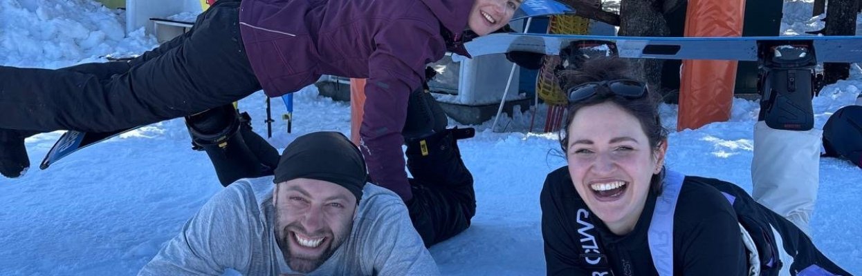 Drie wintersporters lachen samen in de sneeuw bij het meetingpoint van de skischool.