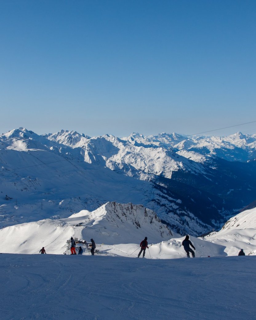 Groep skiërs maakt een afdaling met uitzicht op de besneeuwde bergen.