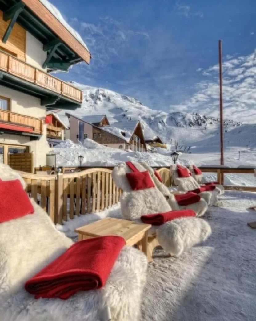 Besneeuwd terras van een berghotel direct aan de piste met uitzicht op de bergen.