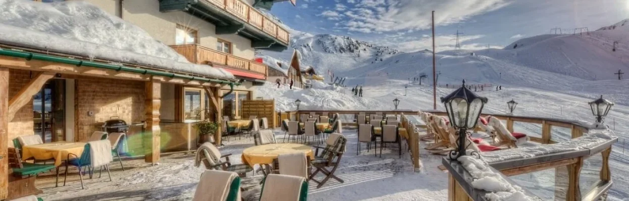 Besneeuwd terras van een berghotel direct aan de piste met uitzicht op de bergen.