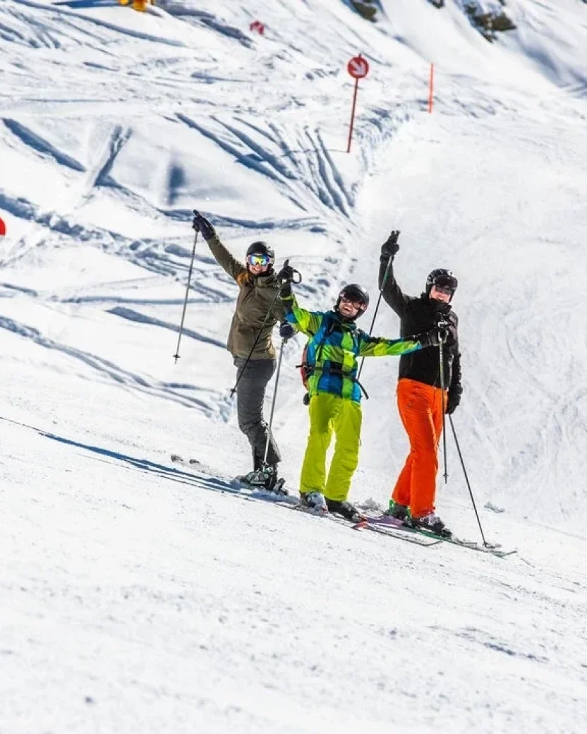 Drie wintersporters poseren samen op de piste met hun ski’s en stokken.