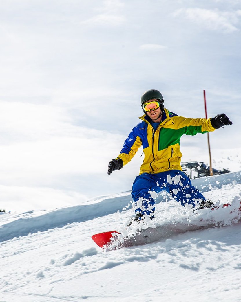 Snowboarder maakt een scherpe bocht door de sneeuw op een zonnige berghelling.