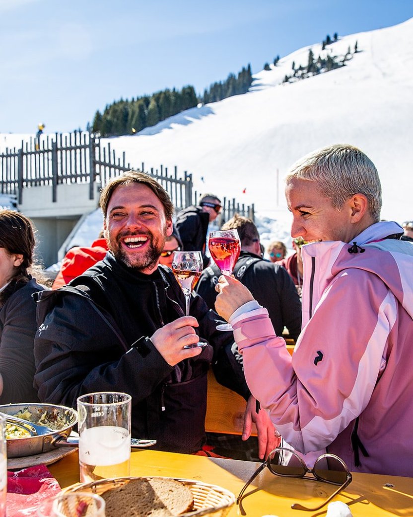 Wintersporters proosten samen op een zonnig terras aan de piste.