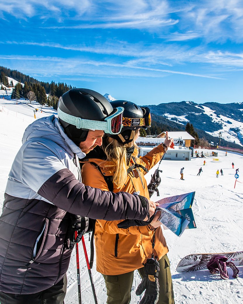 Twee wintersporters bekijken samen de pistekaart op een zonnige berghelling.