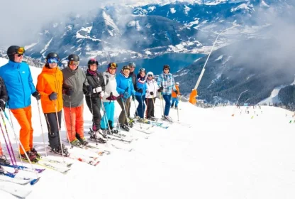 Groep skiërs poseert samen op de piste met uitzicht op het bergmeer en de besneeuwde bergen.