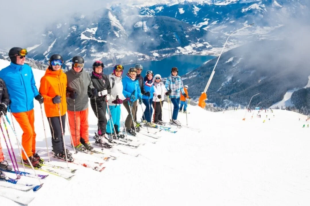 Groep skiërs poseert samen op de piste met uitzicht op het bergmeer en de besneeuwde bergen.