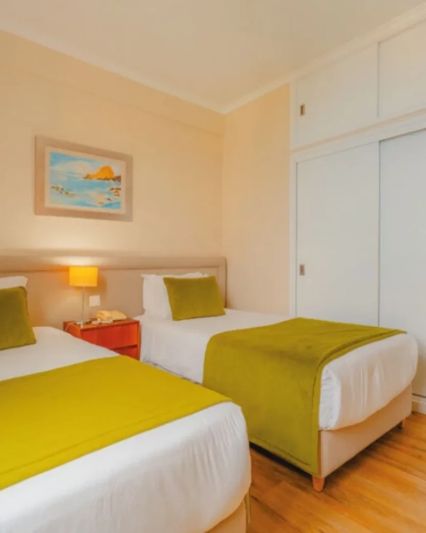 Lichte hotelkamer met aparte bedden en zitkamer.