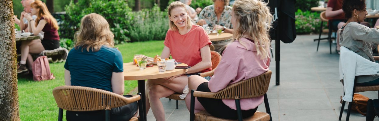 Drie reisgenoten zitten samen buiten aan tafel tijdens een zonnige lunch in het groen.
