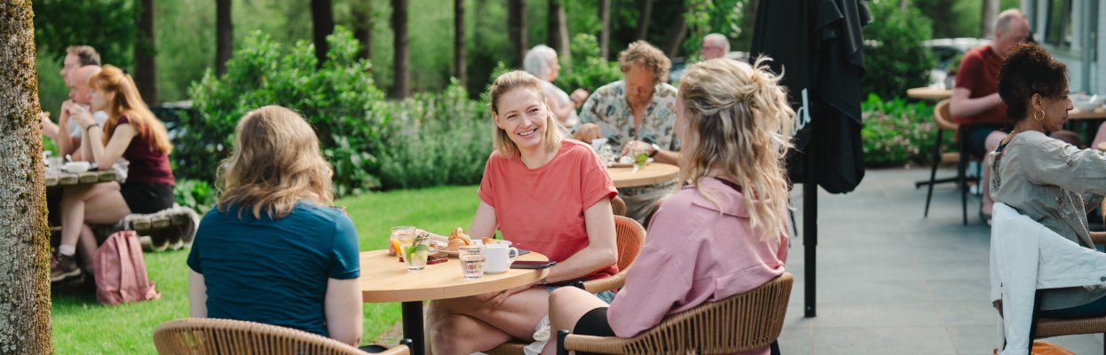 Drie reisgenoten zitten samen buiten aan tafel tijdens een zonnige lunch in het groen.