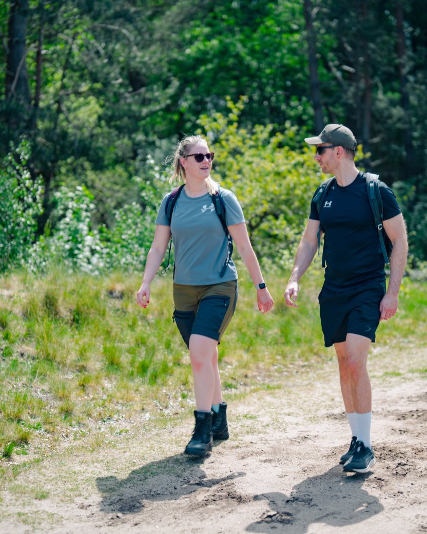 Twee reisgenoten wandelen samen over een zonnig pad door de natuur.