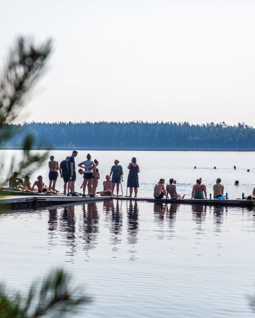 Reisgenoten ontspannen op de steiger en zwemmen in het water met bos op het achtergrond.