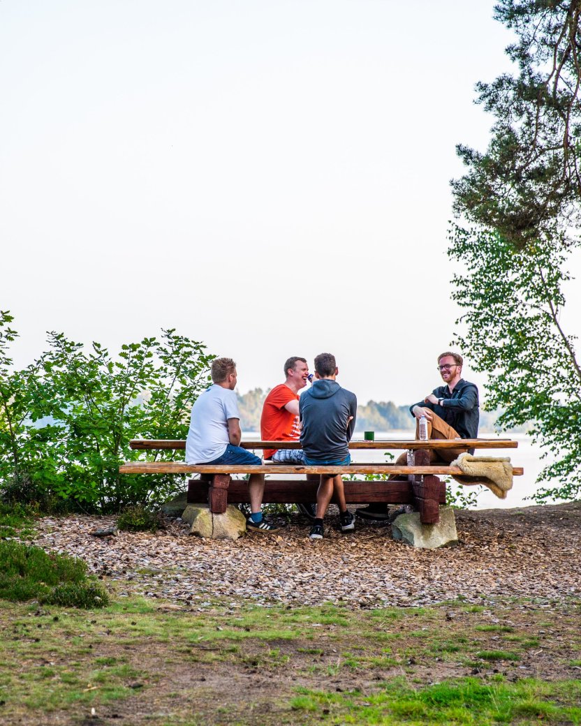 Vier reisgenoten genieten van een drankje aan de picknicktafel naast het meer.