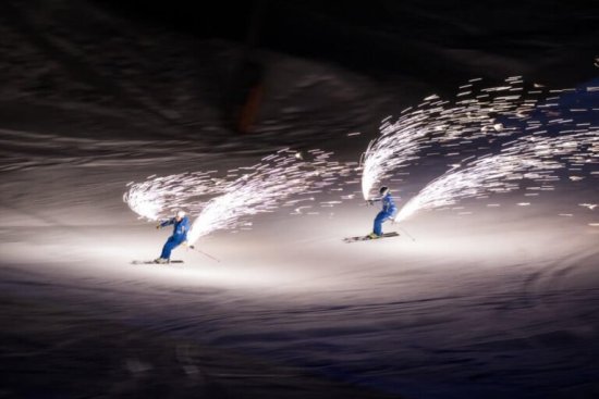 Skiërs maken een afdaling met vuurwerk tijdens een avondshow.