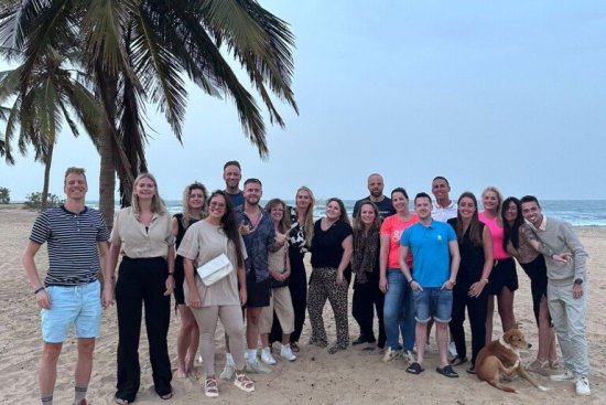 Groep reisgenoten poseert op het strand voor de groepsfoto in Gambia.