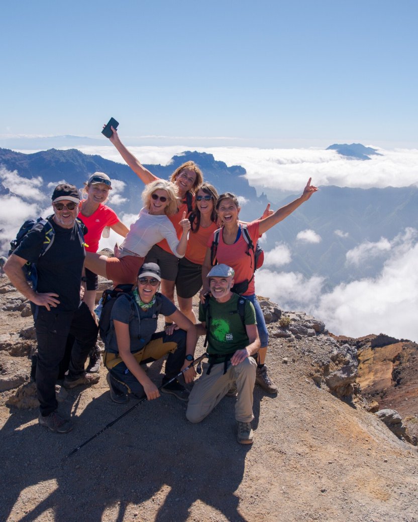 Groep reisgenoten poseren boven op de berg met uitzicht over de andere toppen en het wolkendek.