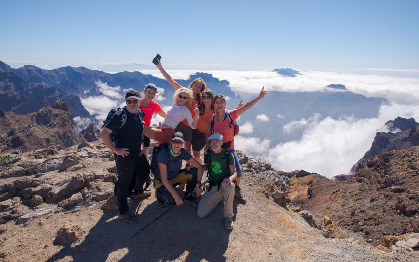 Groep reisgenoten poseren boven op de berg met uitzicht over de andere toppen en het wolkendek.