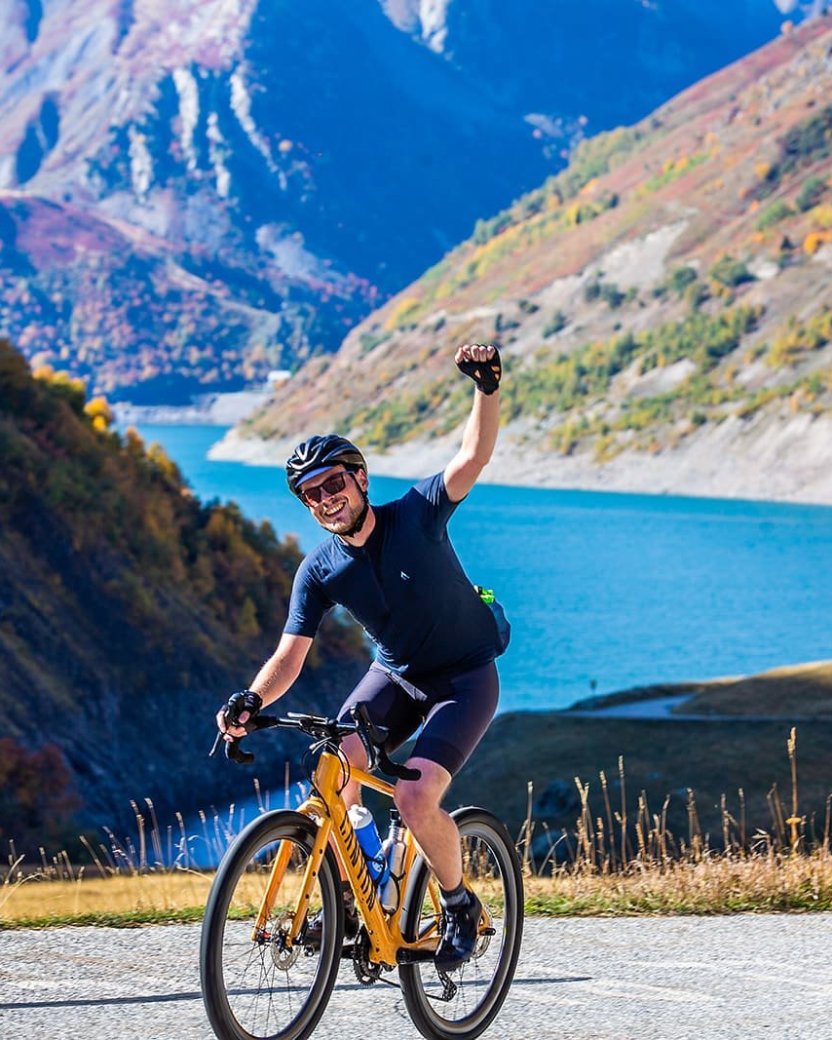 Reisgenoot fietst over de berg met blauw water op het achtergrond.