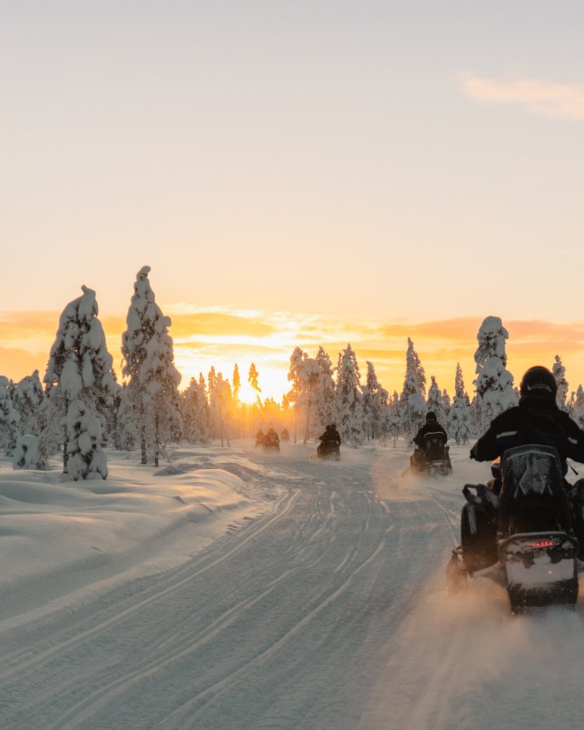Reisgenoten op de sneeuwscooter tijdens zonsondergang in Lapland.