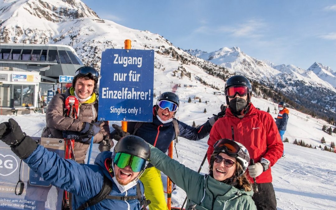 Reisgenoten poseren op de piste bij een skibord waar 'singles only' op staat.
