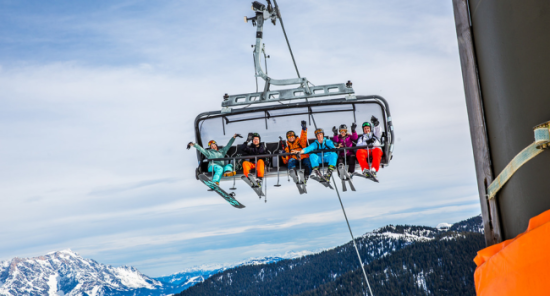 Reisgenoten zitten in de skilift en poseren voor de foto met besneeuwde bergen op het achtergrond.