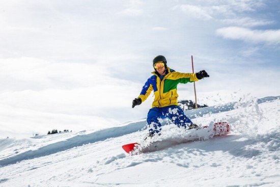 Snowboarder maakt een scherpe bocht door de sneeuw op een zonnige berghelling.