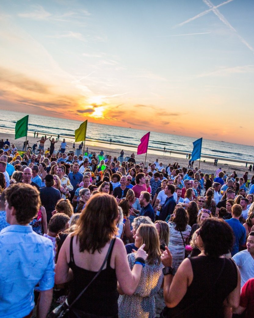 Grote groep reisgenoten op een strandfeest in Nederland bij zonsondergang.